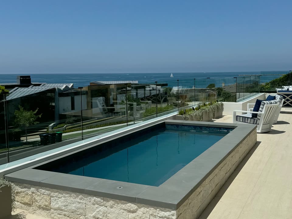 Raised stone-clad plunge pool with glass fencing and ocean views in Newport Beach, CA
