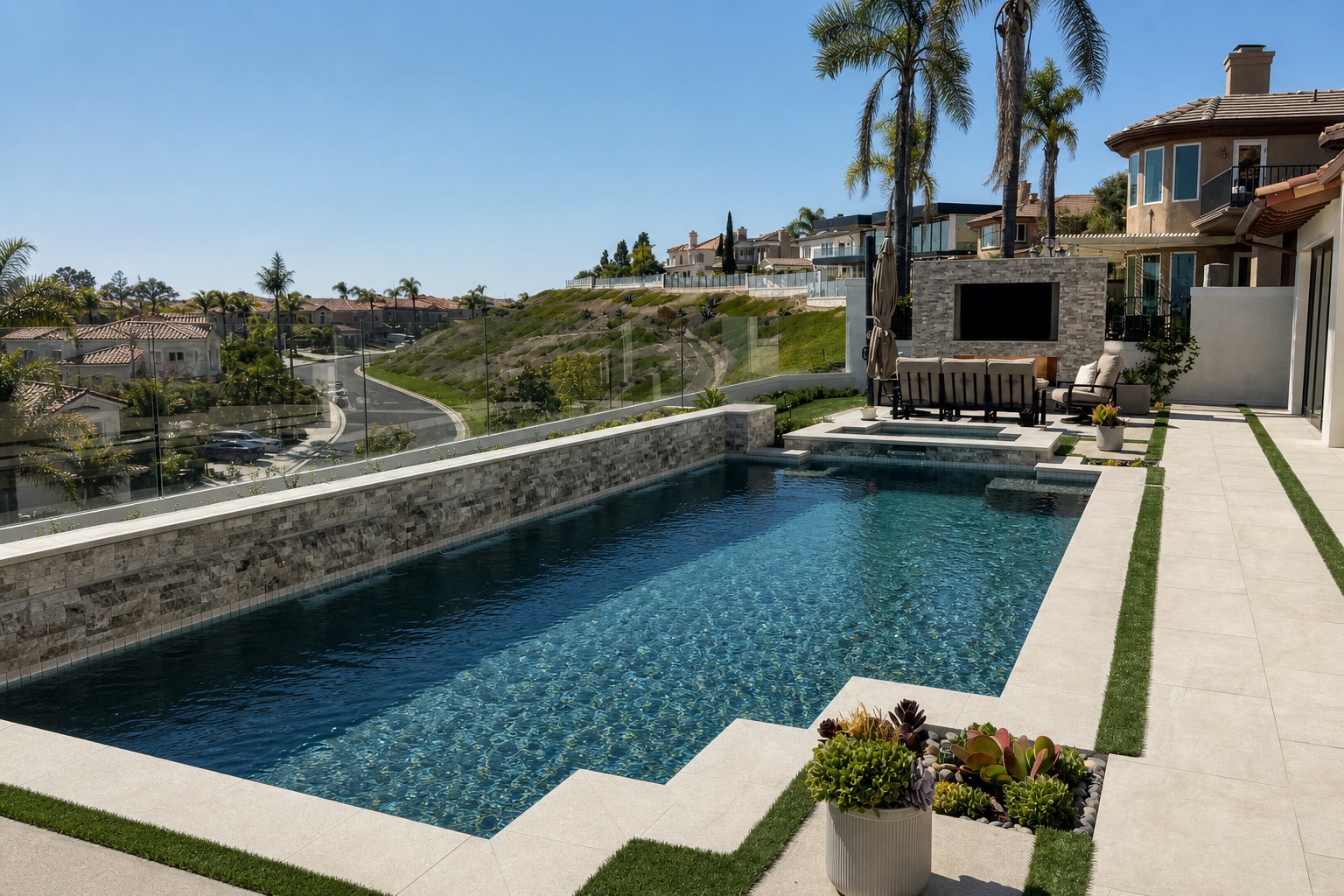 Geometric pool with raised stacked-stone wall, glass fencing and outdoor lounge with TV overlooking the hills in Laguna Niguel, CA