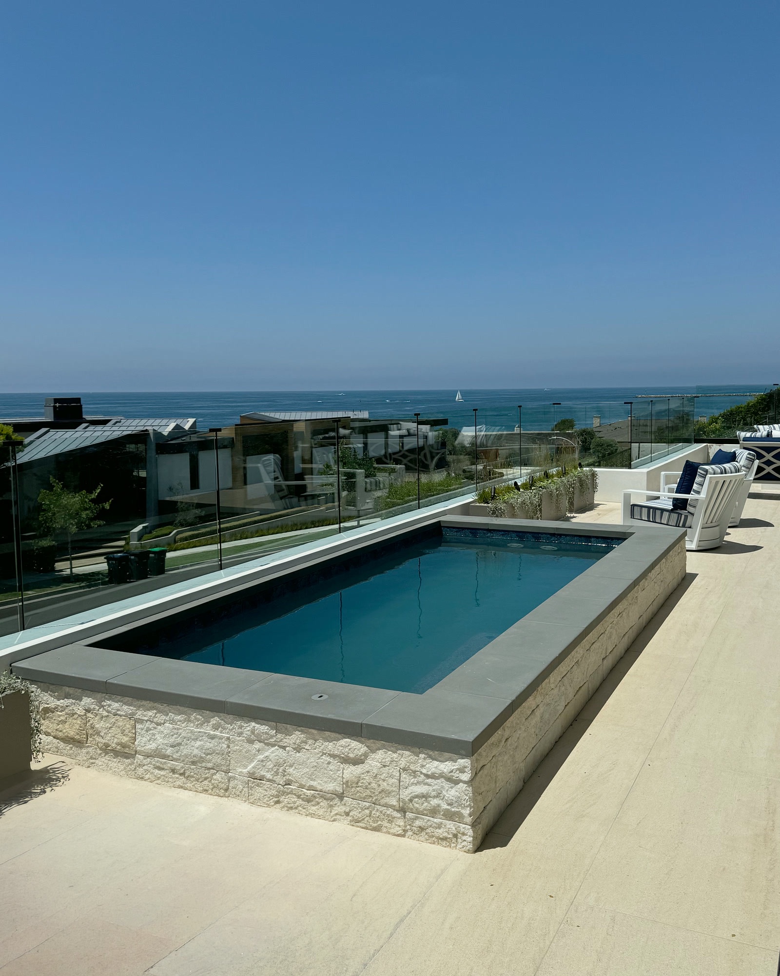 Raised stone-clad plunge pool with glass fencing and ocean views in Newport Beach, CA