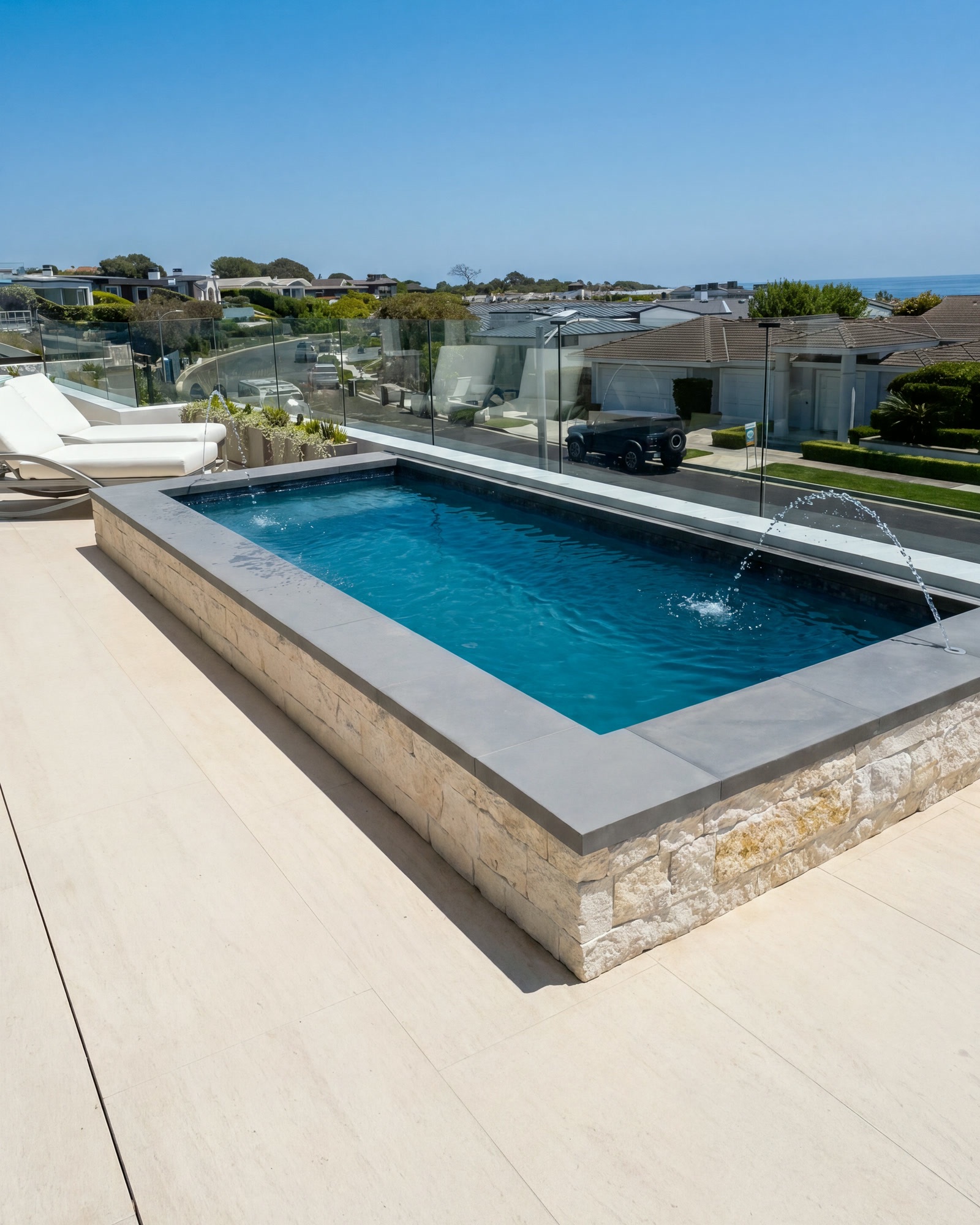 Raised pool with arcing deck jets, loungers and glass fencing overlooking the coast in Newport Beach, CA